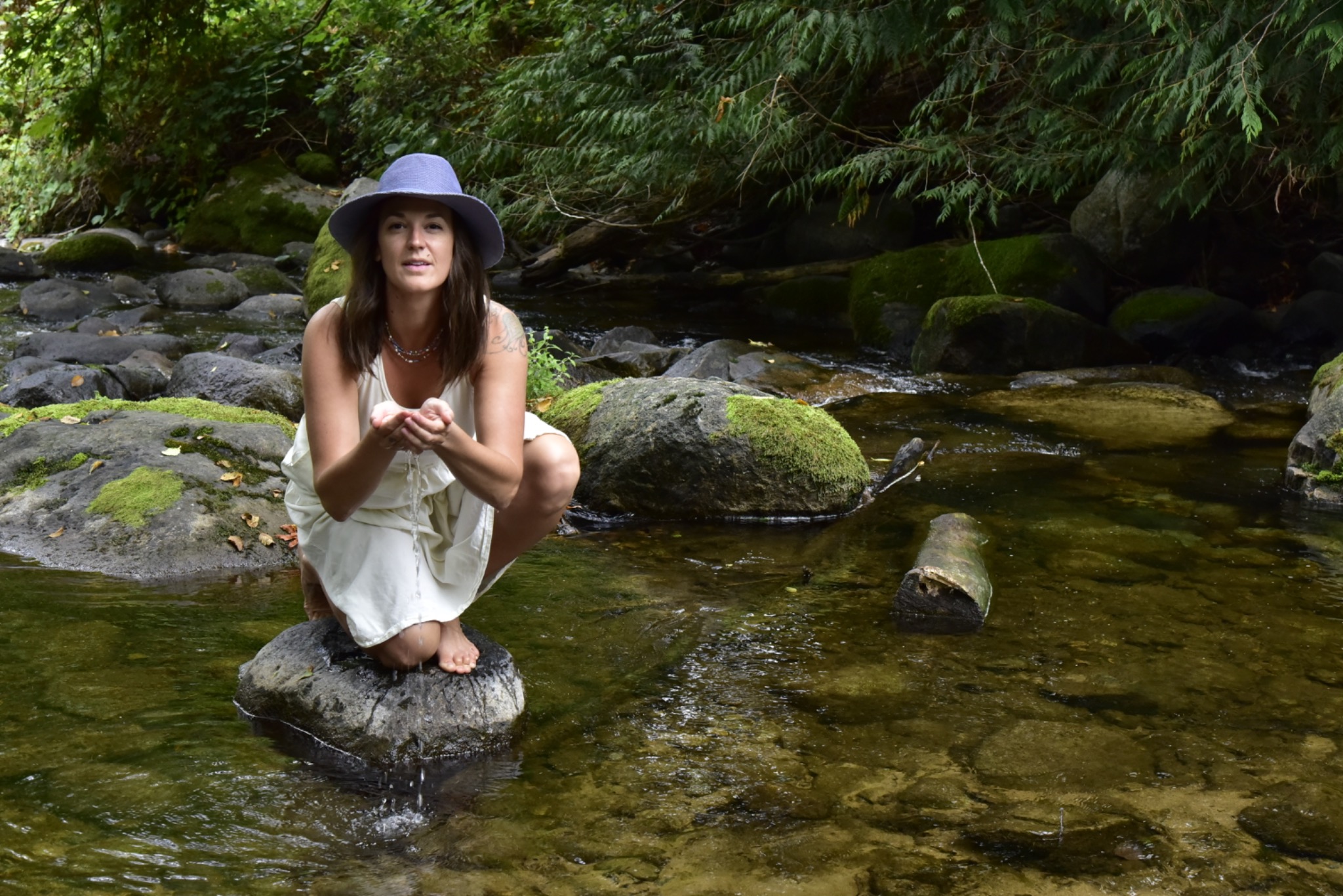 Alix holding water in her hands beside a forest creek